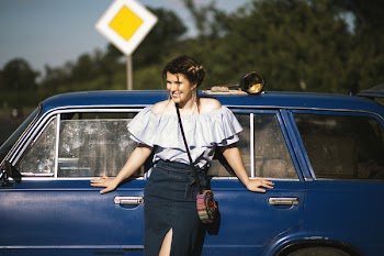 Woman Wearing White Off-shoulder Top While Touching Blue Car