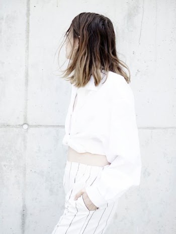 woman wearing white shirt and pants standing beside wall looking sideways