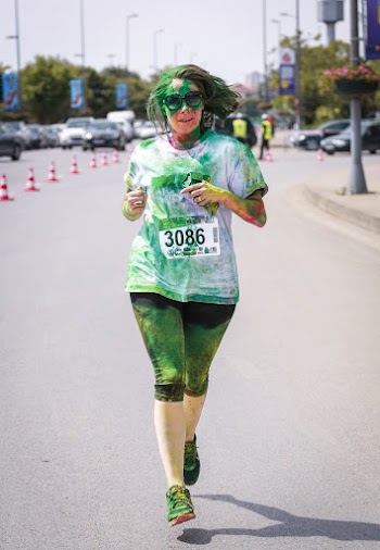 Woman Wearing White Shirt Covered With Green Powder While Jogging on Road