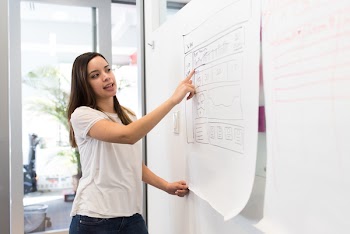Woman Wearing White Shirt Standing Beside White Board While Pointing on White Paper