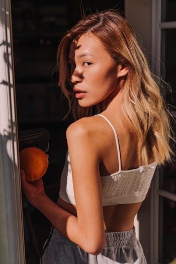 woman wearing white spaghetti strap crop top and holding orange fruit