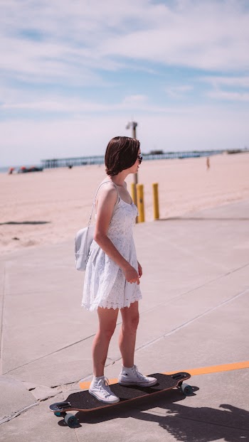 Woman Wearing White Spaghetti Strap Dress Standing on Black Skateboard Under White and Blue Sky