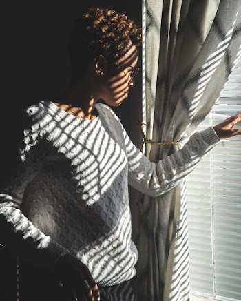 Woman Wearing White Sweater Standing in Front of Window Blinds