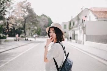 woman wearing white T-shirt and blue backpack standing on road