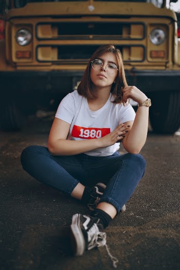 Woman Wearing White T-shirt Sitting on the Ground in front of a Yellow Bus