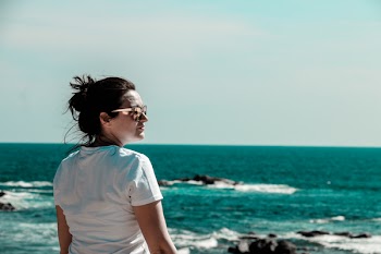 Woman Wearing White T-shirt With Distance at Sea With Rock Formations