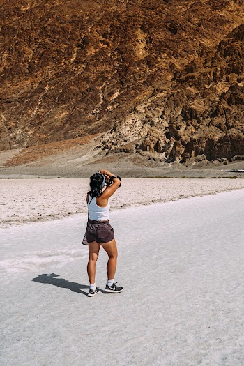Woman Wearing White Tank Top and Brown Short-shorts Taking Photo of Brown Cliff
