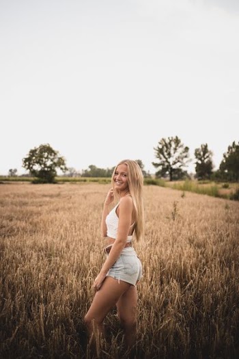 woman wearing white tank top and gray denim short shorts standing on wheat field during daytime