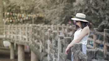 Woman Wearing White Tank Top and White Hat Standing on a Boardwalk