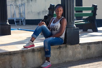 Woman Wearing White Tank Top Leaning on Post Sitting on Concrete Pavement