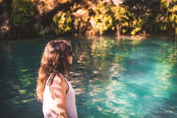 woman wearing white tank top walking beside body of water during daytime