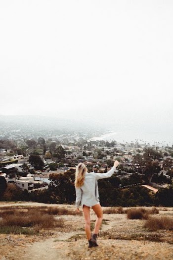 woman wearing white top standing on brown field overlooking town