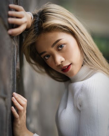 Woman Wearing White Turtle-neck Long-sleeved Shirt While Leaning On Concrete Wall