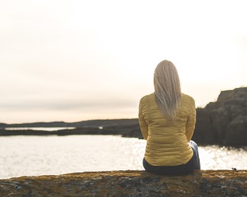 Woman Wearing Yellow Bubble Jacket Sitting in Front of Sea