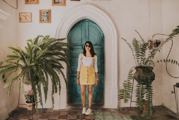 Woman Wearing Yellow Dungaree Skirt Standing in Front of Green Wooden Door