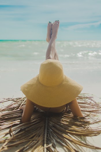 Woman Wearing Yellow Hat With Feet Raised Sunbathing on Shore