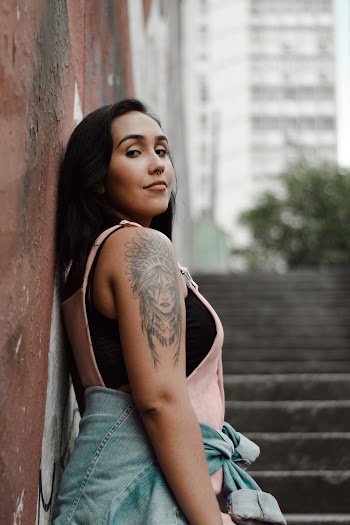 Woman With Arm Tattoo Leaning on Brown Wall