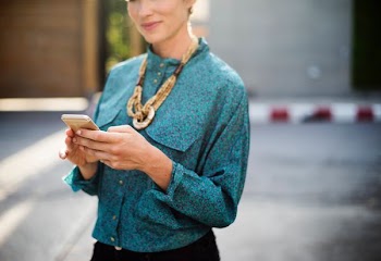 woman with brown necklace holding gold smartphone