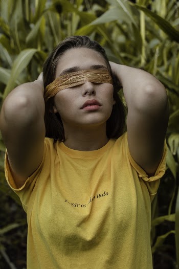 Woman With Brown Tape on Eyes Wearing Yellow Shirt Standing Beside Green Plants