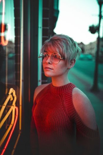 woman with eyeglasses looking at glass panel with neon signage