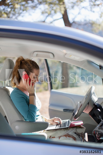 Woman with laptop and smart phone working inside car