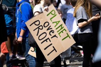 Women Holding a Planet over Profit Sign