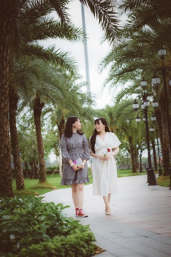 Women Walking on Concrete Pavement Between Trees