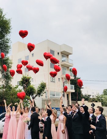 Women Wearing Pink Dresses and Men Wearing Black Suit Jacket and Pants Raising Hands With Red Heart Balloons