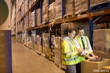 Worker and manager meeting at laptop in aisle of distribution warehouse