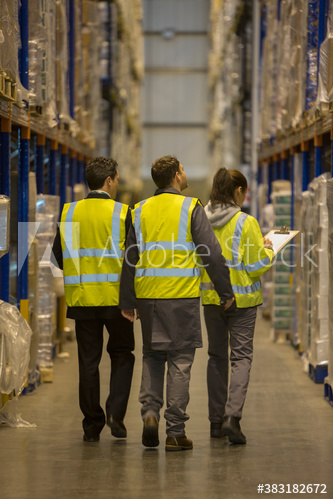 Workers in reflective vests in aisle of distribution warehouse