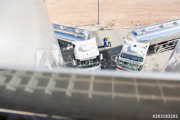 Workers talking between milk tankers on sunny dairy farm