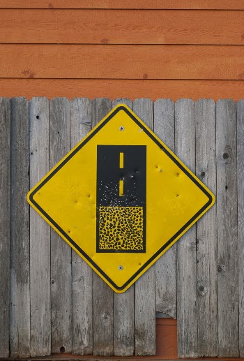 Yellow and Black Road Sign on Gray Wooden Fence