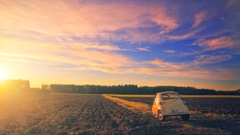 Yellow Classic Car Parked on Field Under Cloudy Sky at Golden Hour