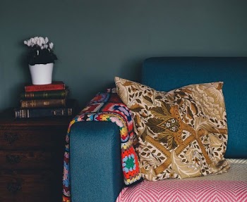 yellow throw pillow on blue couch beside on pile of books on top of drawer
