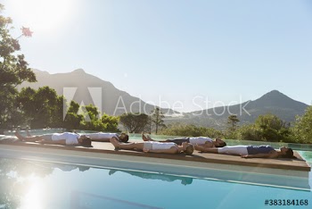 Yoga class practicing corpse pose at sunny poolside