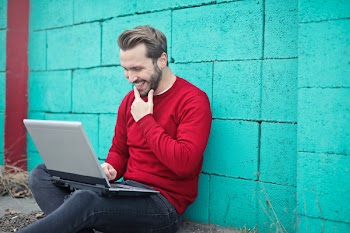  Young Adult Man using a laptop against turquoise brick wall 