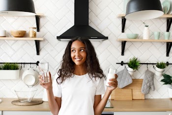 Young afro girl holds two glasses with water and milk and thinks what choice to make Free Photo