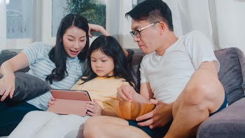 Young asian family and daughter happy using tablet at home. japanese mother, father relax with little girl watching movie lying on sofa in living room. funny parent and lovely child are having fun. Free Photo