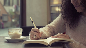young beautiful woman writing on her diary and drinking cappuccino ...