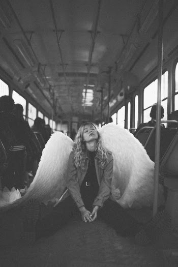 Young Blond Woman Disguised as Angel Kneeling on Bus with Hands Clasped · Free Stock Photo