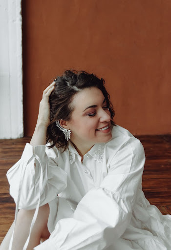 Young Brunette in a White Shirt Sitting with Her Hand in Hair and Smiling