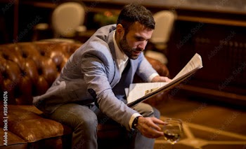 Young businessman drinking wine and reading newspaper in the office