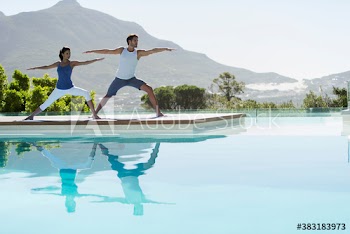 Young couple practicing yoga warrior 2 pose at sunny poolside
