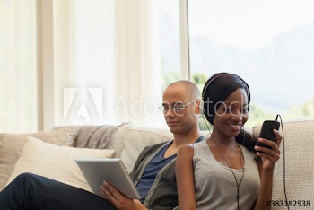 Young couple using digital tablet and listening to music on sofa