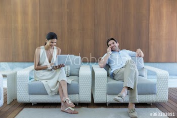 Young couple using laptop and smart phone in armchairs