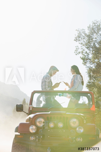 Young couple using smart phones in sunny jeep