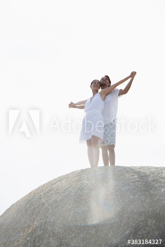 Young couple with arms outstretched on sunny rock
