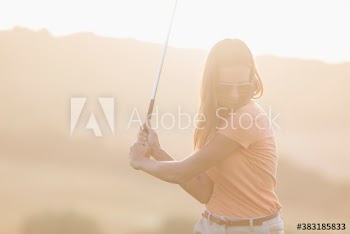Young female golfer swinging golf club on sunny golf course