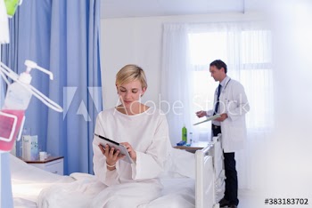 Young female patient using digital tablet on edge of hospital bed