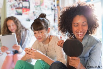 Young female roommates putting on makeup and using technology